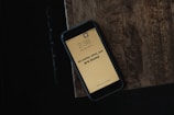 A smartphone rests on a wooden surface, displaying the time as 2:38 on Saturday, May 5. The screen shows the message 'No matter what, you are loved' on a light background.