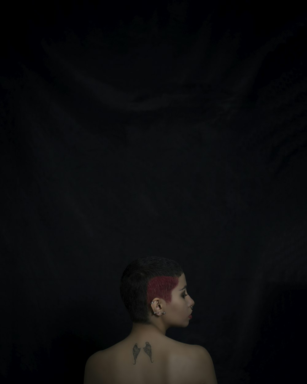 mulher com cabelo vermelho e preto e asa de tatuagem nas costas