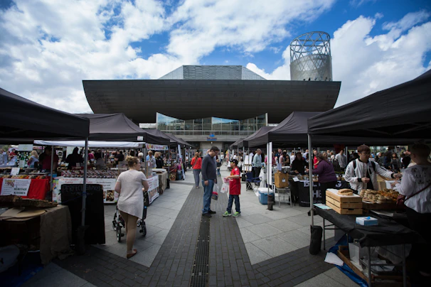 A sleek German-style canopy tent in a busy commercial market setting, sheltering vendor stalls under a bright blue sky.