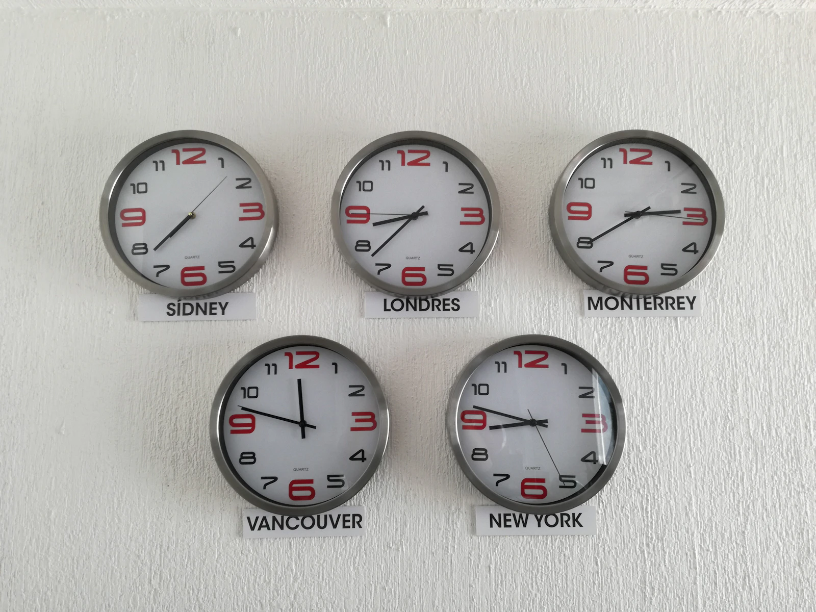 A row of wall clocks labelled with cities in different timezones