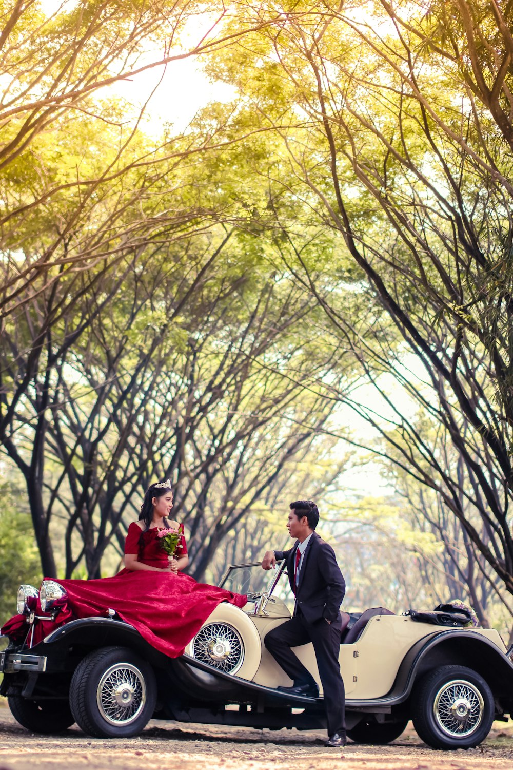 Bräutigam und Braut auf Oldtimer umgeben von Bäumen