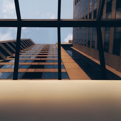 An upward view of a glass skyscraper with reflections of emerging markets trading floors.