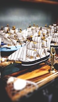 A collection of finely detailed miniature sailing ships with striped sails is arranged on a wooden surface. The ships are crafted with attention to detail featuring dark hulls and light-colored sails. Some golden elements are visible, contributing to the decorative aspect.