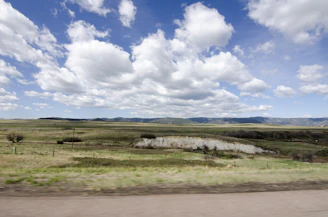 Spacious open land plot bordered by a dirt road and distant hills under a bright sky.