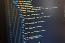 A computer monitor displays HTML code in an integrated development environment. The screen shows a structured hierarchy of HTML tags, including elements such as header, nav, and list items with classes and hyperlinks.