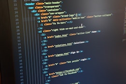 A computer monitor displays HTML code in an integrated development environment. The screen shows a structured hierarchy of HTML tags, including elements such as header, nav, and list items with classes and hyperlinks.