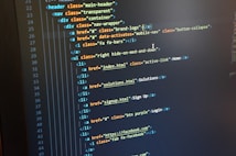 A computer monitor displays HTML code in an integrated development environment. The screen shows a structured hierarchy of HTML tags, including elements such as header, nav, and list items with classes and hyperlinks.