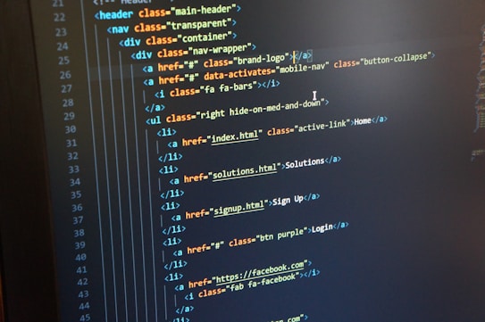 A computer monitor displays HTML code in an integrated development environment. The screen shows a structured hierarchy of HTML tags, including elements such as header, nav, and list items with classes and hyperlinks.