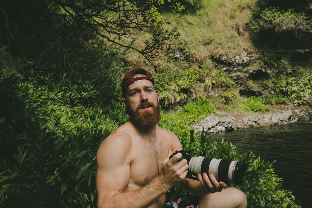 man holding camera beside body of water