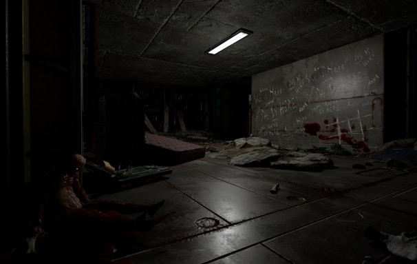 A dimly lit, sinister room with a concrete ceiling and floor, featuring scattered debris and a mattress. Graffiti and red marks resembling bloodstains cover one wall. A humanoid figure slumps against a wall, adding to the eerie atmosphere, while a flickering overhead light casts shadows.