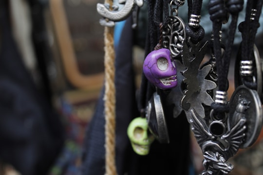 Various pendants and charms hang on black cords, including skull-shaped and ornate metallic designs. The focus is on a purple skull pendant, surrounded by intricate metallic figures and shapes.