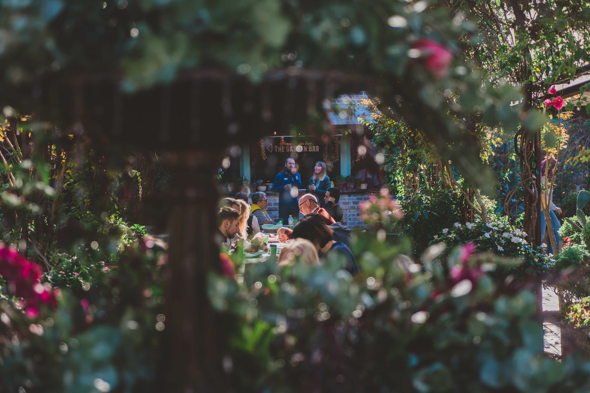 Guests enjoying a sunny afternoon at garden-ia, seated comfortably with drinks in hand amidst the peaceful garden setting.