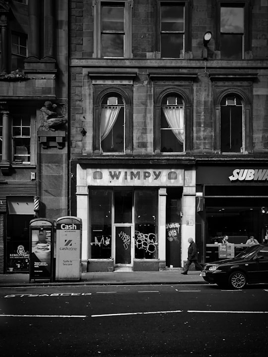 grayscale photo of person waking on street beside Wimpy boutique in Glasgow United Kingdom