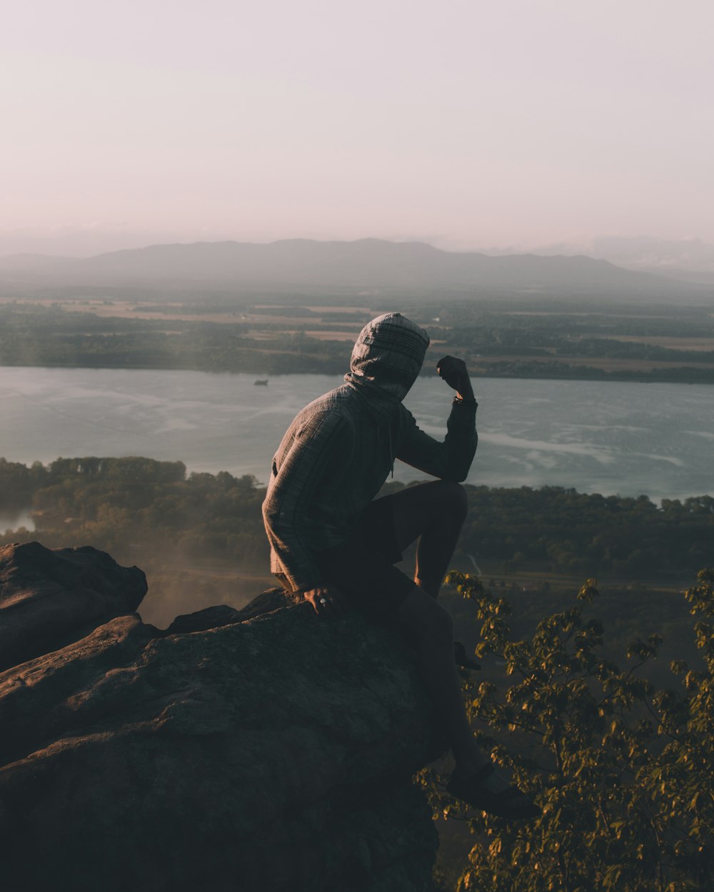 man sitting on cliff over body of water