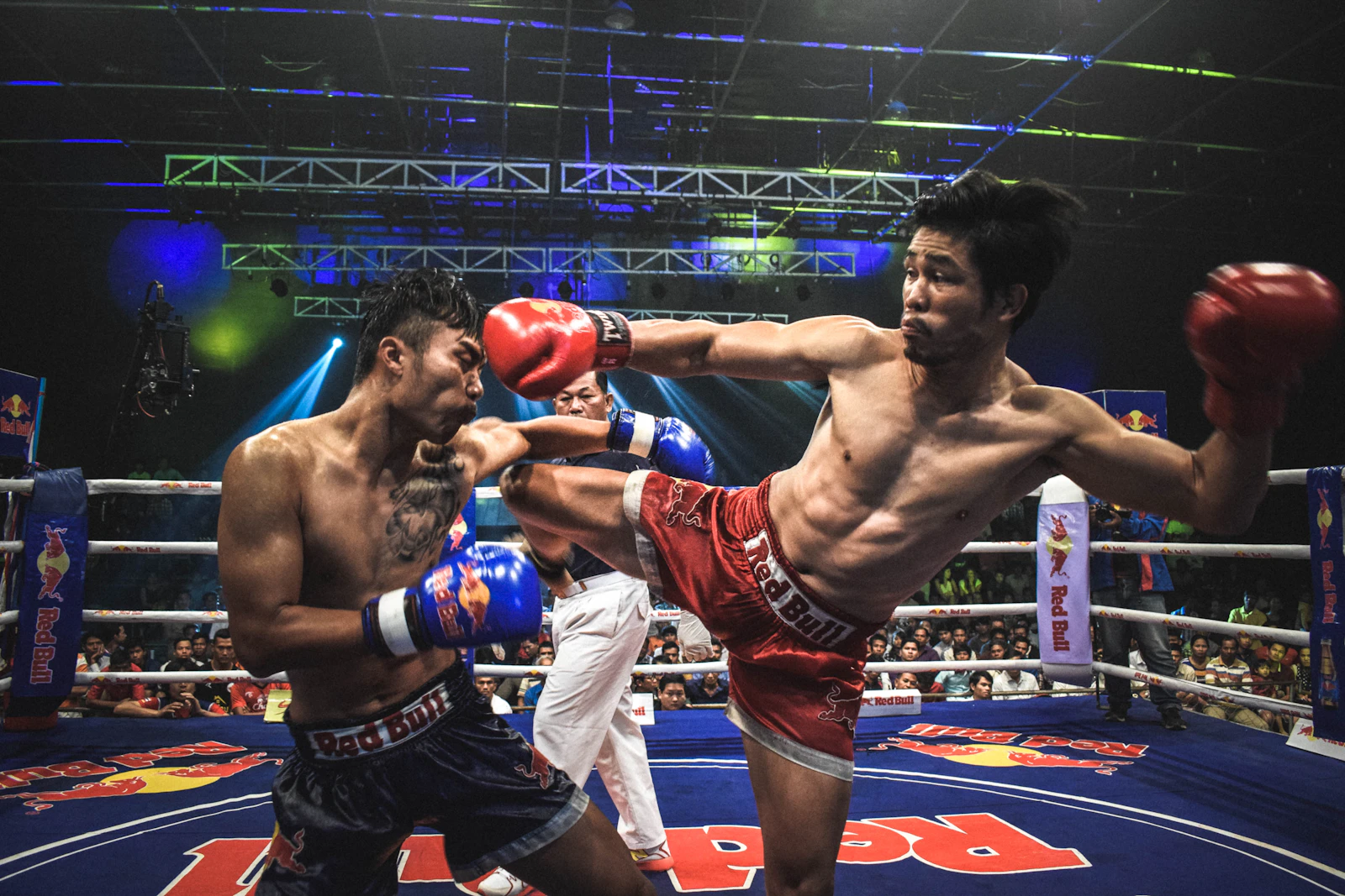 A fighter landing a roundhouse kick in a Muay Thai stadium fight