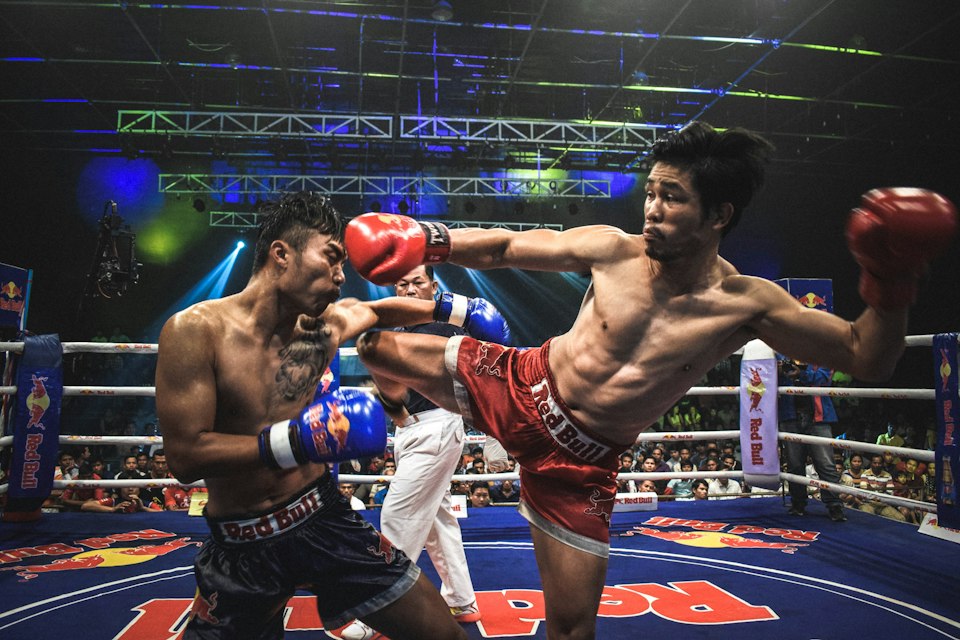 Two Muay Thai fighters exchanging a high kick under bright stadium lights