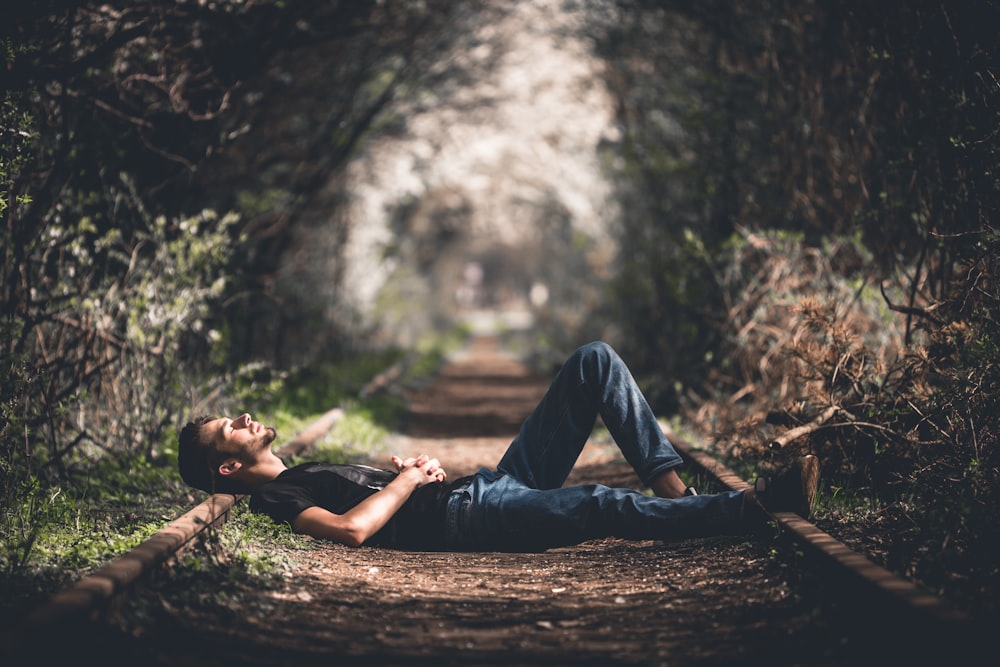 focus photography of man lying on pathway with plants