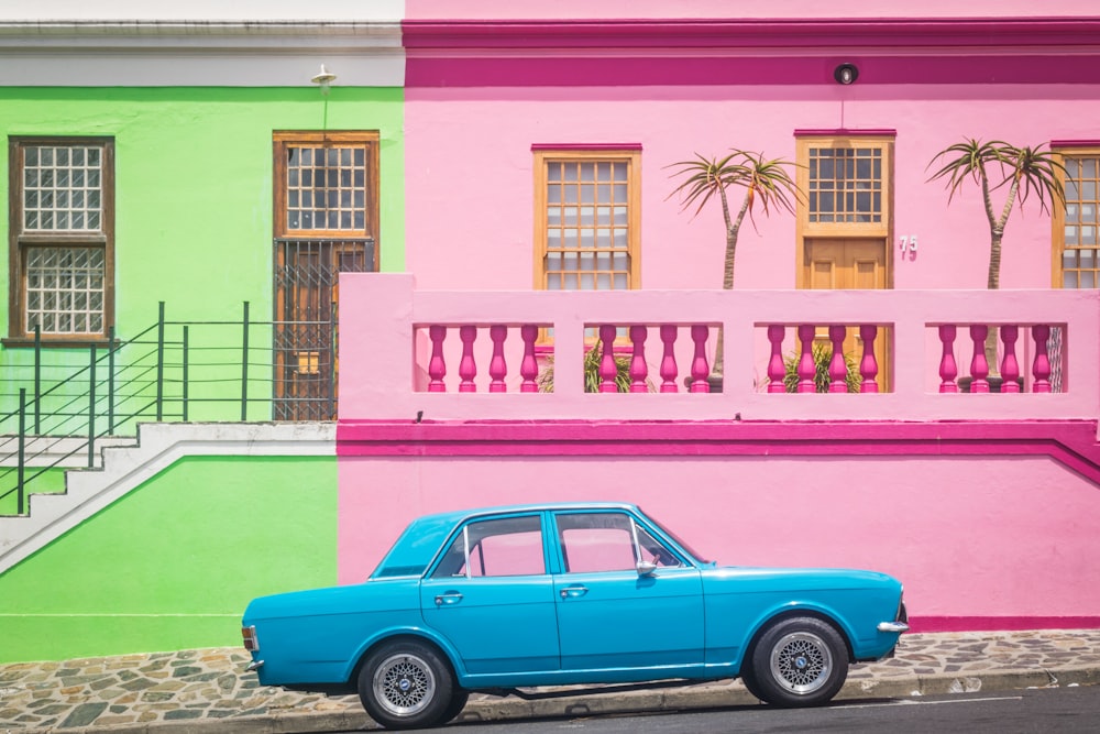 blue coupe in front of pink house