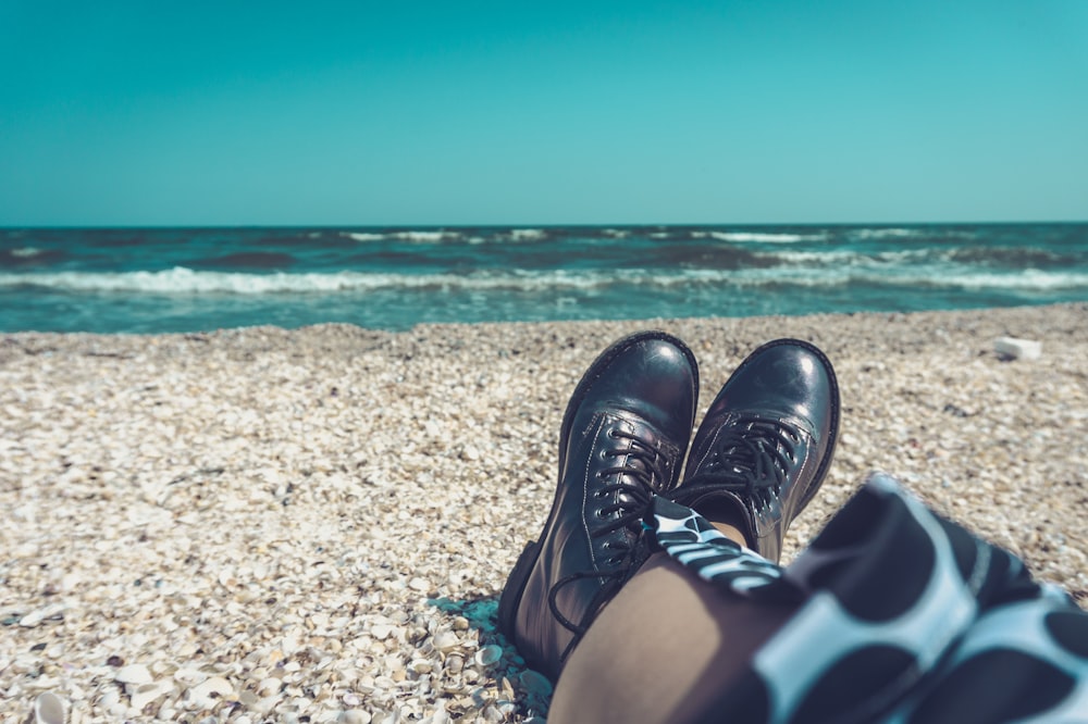 person wearing pair of black leather shoes sitting on seashore