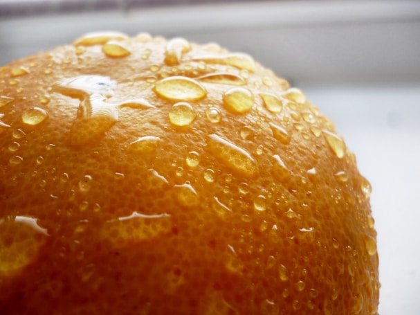 Close-up view of an orange peel covered with water droplets, highlighting the textured surface and juicy freshness.