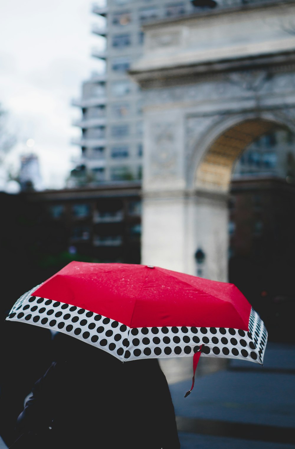 person under red and white umbrella walking near building