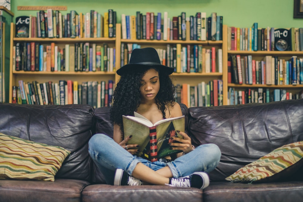 mulher lendo um livro enquanto sentada no sofá de couro preto de 3 lugares