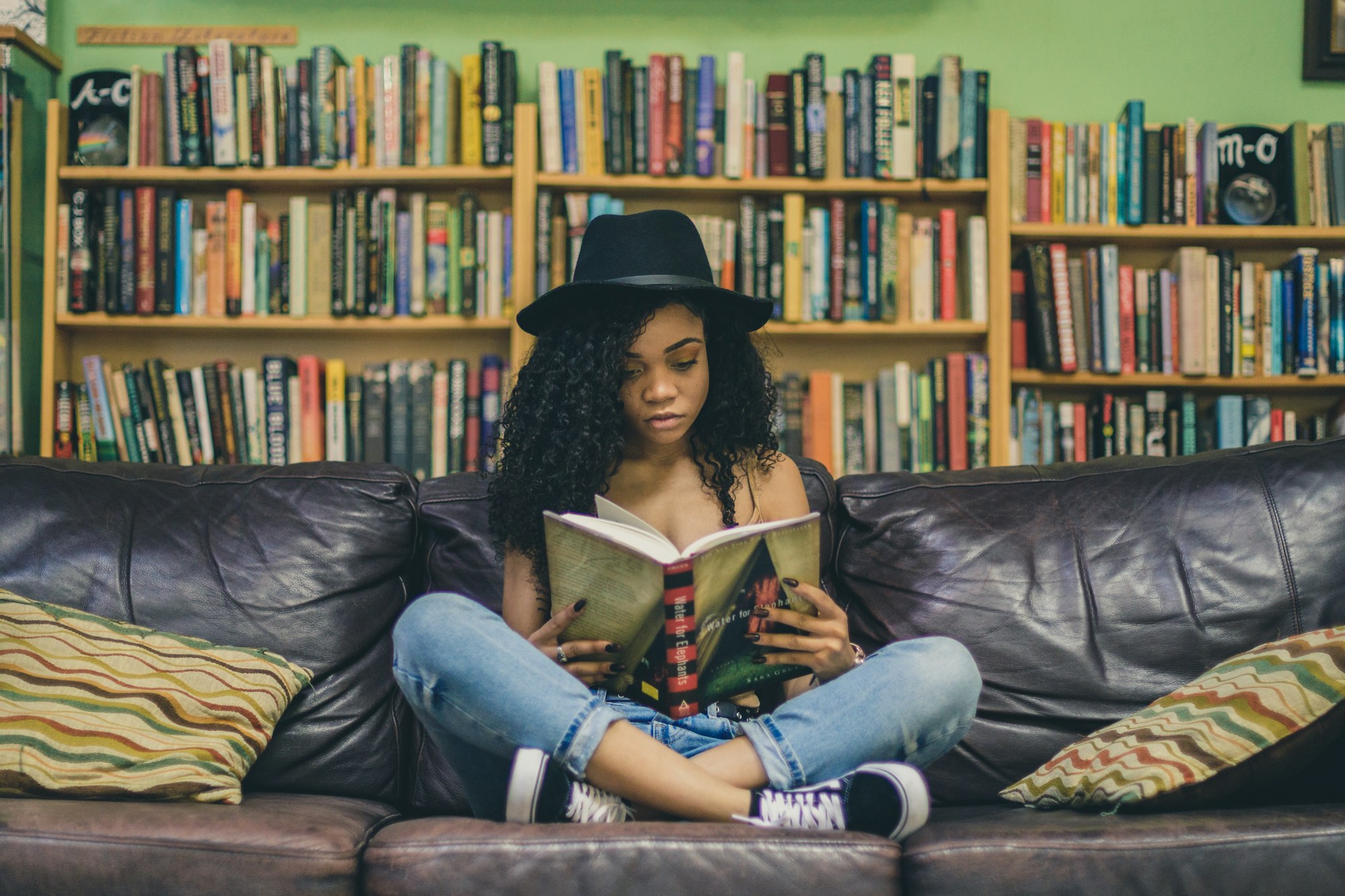 A woman reads a large book while sitting cross-legged on a leather couch.