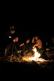 A group of men engaged in heartfelt discussion around a campfire at dusk.