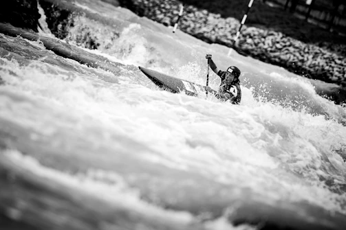 Athlete in vibrant hydtec kayak gear paddling fiercely through whitewater rapids.