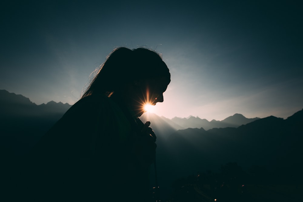 日没時に山の頂上に立っている女性のシルエット
