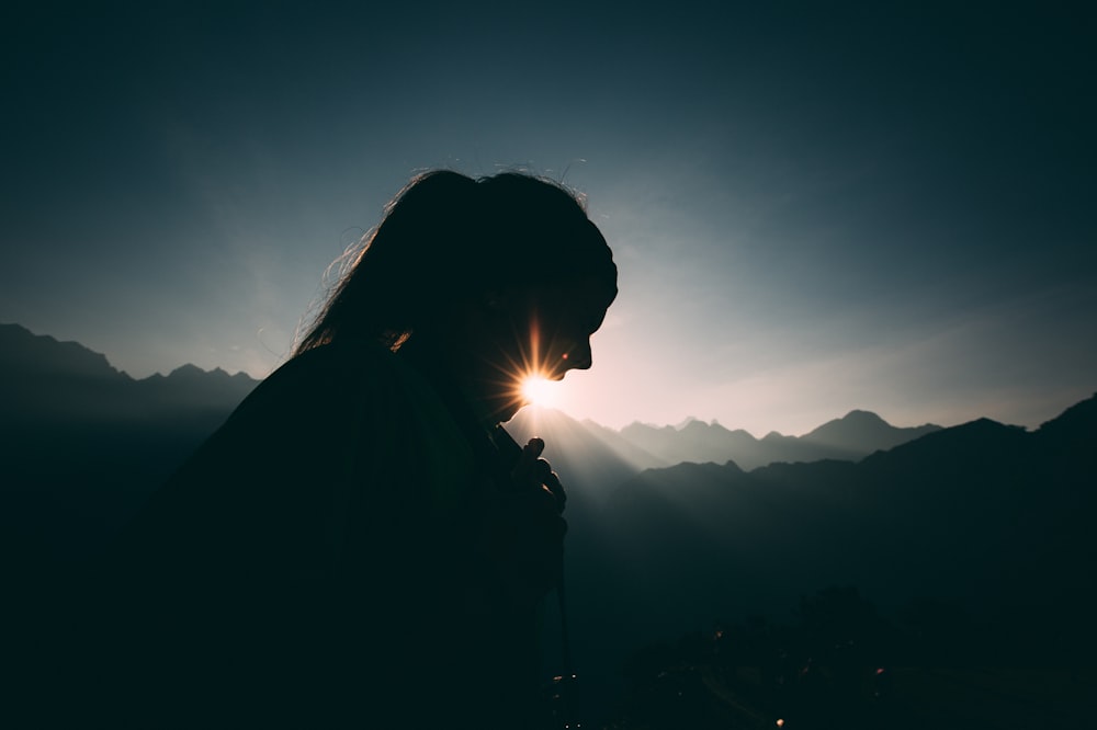 silhouette of woman standing on top of mountain during sunset