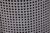 A close-up view of a perforated metal surface with evenly spaced circular holes, giving a textured and industrial appearance.