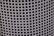 A close-up view of a perforated metal surface with evenly spaced circular holes, giving a textured and industrial appearance.