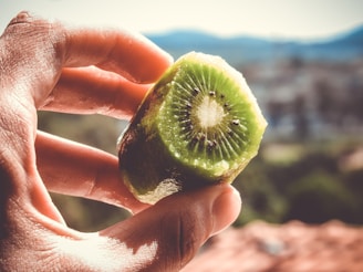 A close-up of hands exchanging a small kiwi fruit with a backdrop of financial charts.