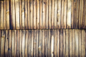 Wooden planks aligned vertically, displaying a weathered and natural appearance. The surface shows a range of tan to dark brown hues with visible knots and grain patterns.