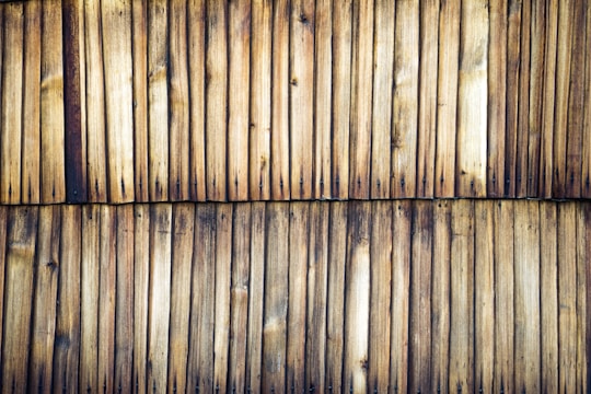 Wooden planks aligned vertically, displaying a weathered and natural appearance. The surface shows a range of tan to dark brown hues with visible knots and grain patterns.