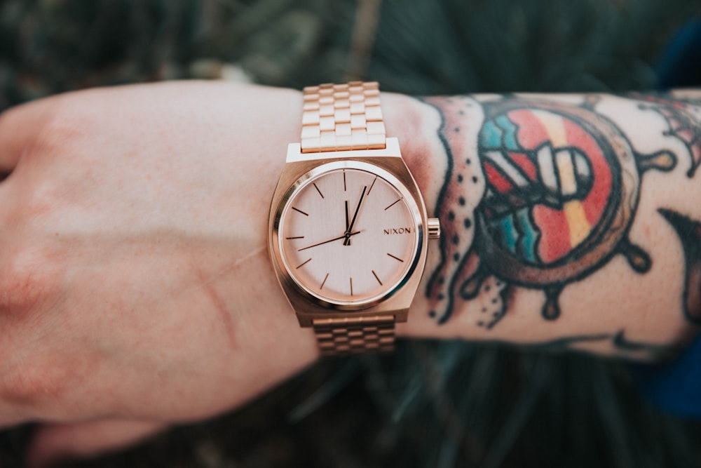 person wearing round gold-colored analog watch display at 12:04 o'clock