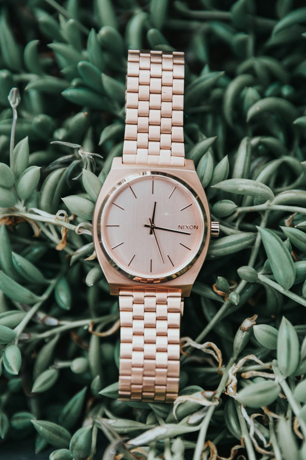 round gold-colored Nixon analog watch with link bracelet