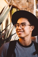 smiling man wearing black framed eyeglasses and hat
