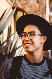 smiling man wearing black framed eyeglasses and hat