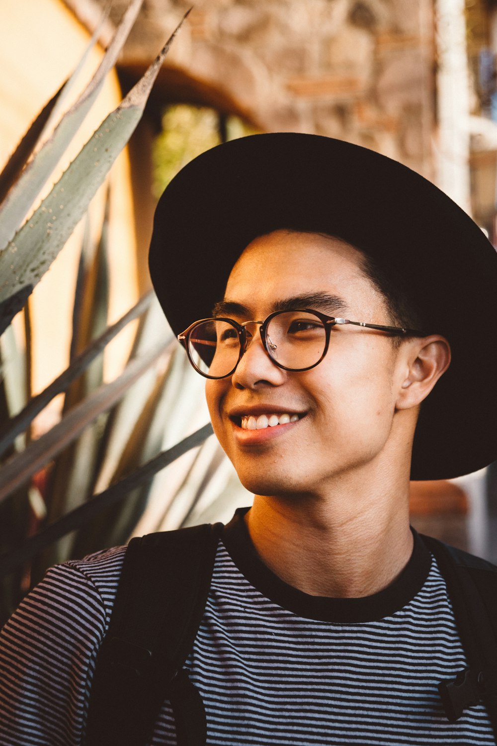 Homme souriant portant des lunettes et un chapeau à monture noire