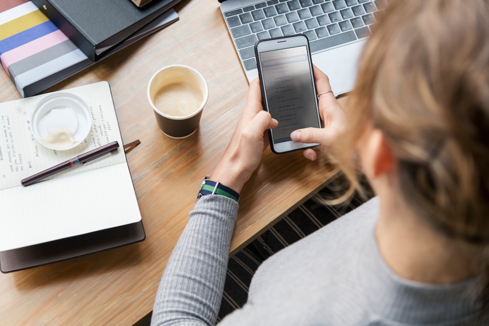 woman operating smartphone in front of laptop and cup of coffee