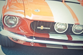 A classic car with a vintage design, featuring a prominent front grille, dual round headlights, and a distinctive orange and white striped pattern.
