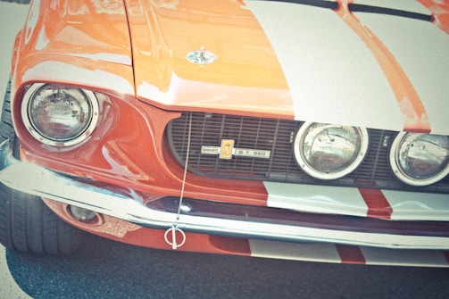 A classic car with a vintage design, featuring a prominent front grille, dual round headlights, and a distinctive orange and white striped pattern.