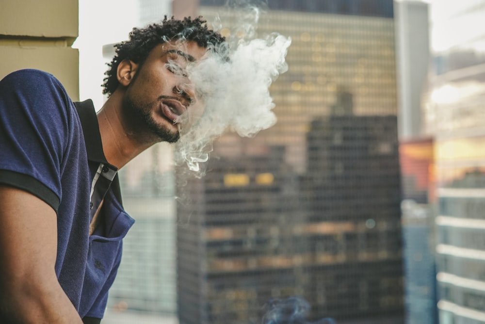 man in blue and black polo shirt blowing smoke