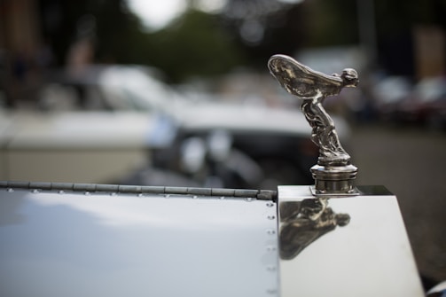 Close-up shot of a shiny vintage car hood ornament reflecting the crowd.