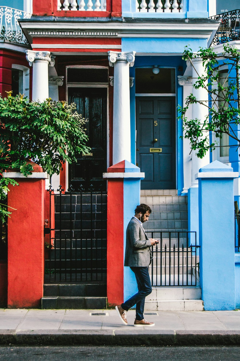 man using smartphone passing by blue and red houses
