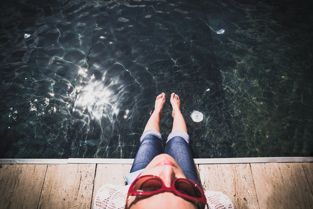 woman sitting on brown platform with her feet at body of water