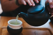 Close-up of hands preparing tea with delicate teapot and cups.