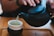 A hand pouring tea from a classic Yixing teapot into a small porcelain cup on a wooden tray.